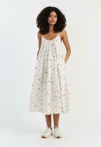 Abito maxi senza maniche in crema con stampa floreale colorata. Presenta una scollatura arricciata e tasche, abbinato a sneakers bianche.