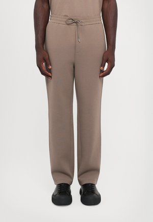 Beige sweatpants with an elastic waistband and adjustable drawstring detail, featuring a relaxed fit and straight leg design.