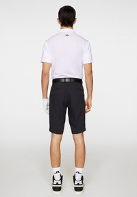 Vit kortärmad polo med en svart logga vid nacken, kombinerad med svarta shorts och vita strumpor med en svart logga, samt svarta sneakers.