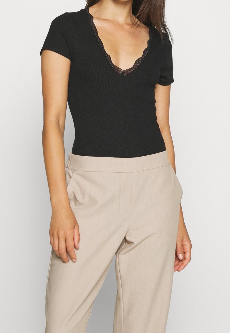Svart, ribbad bodysuit med djup V-ringning och spetsdetaljer, kombinerad med beige högmidjade byxor. Slät tyg, åtsittande design.