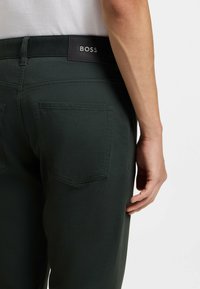 Pantaloni verdi in cotone con taglio dritto, caratterizzati da una toppa con il logo BOSS nero sulla vita e due tasche posteriori.