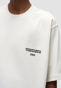 T-shirt in cotone color crema con colletto a girocollo rigato e maniche corte, caratterizzato da un logo stampato nero sul petto.