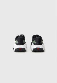 Chaussures de sport noires avec des semelles blanches, une tige texturée, des accents verts à l'arrière et un détail rouge sur le talon.