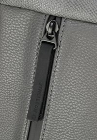 Borsa in pelle grigia con texture, dotata di una zip nera prominente e di un tirante. Il tessuto è liscio con un sottile motivo a grana.