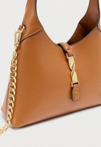 Sac à main en cuir fauve à texture lisse, de forme triangulaire, avec des accents en métal doré et une bandoulière chaîne. Dispose d'une fermeture décorative.