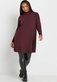 Ribbad, bourgogne klänning med en falsk polokrage, långa ärmar och vågformad nederkant, i kombination med svarta imitation läder leggings och kängor.