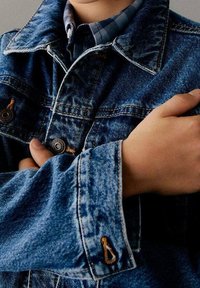 Džínová bunda s klasickým střihem, v modrém odstínu, s velkým límcem, viditelným šitím a kovovými knoflíky. Rukávy mají skládací design.