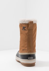 Botín de textil marrón impermeable con un puño blanco esponjoso, suela de goma oscura y marca visible en el lateral y la parte trasera.