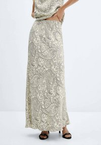 Maxinederdel i lyst beige stof med indviklede sorte paisley-mønstre. Materialet virker blødt med en flydende silhuet og en sideslids.