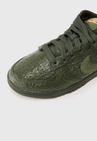 Žalios krokodilo odos tekstūros sportbačiai su raištelių dizainu, turintys perforacijas ant pirštinės ir su velveto Nike swoosh akcentu.