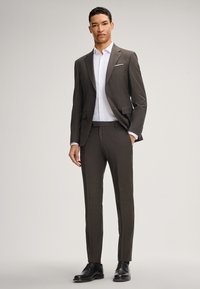 Dunkelgrauer, maßgeschneiderter Anzug mit schlanker Passform, kombiniert mit einem weißen Hemd. Schwarze Schuhe runden den formellen Look ab. Auffällige maßgeschneiderte Details sind vorhanden.