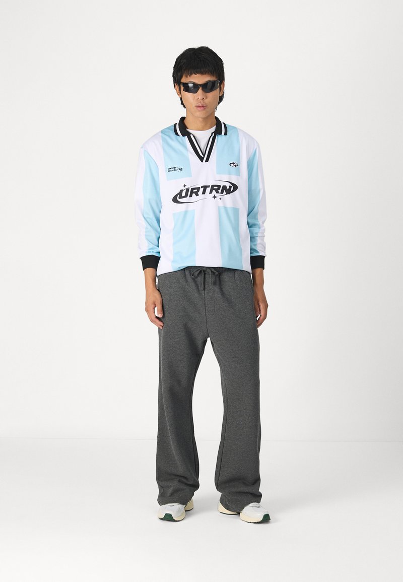 Langermet lys blå og hvit stripete jersey med svart krage, kombinert med mørkegrå joggebukser og hvite sneakers med grønne detaljer.