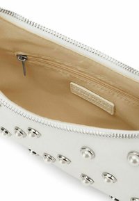 Interno della borsa bianca con zip, foderato in beige, caratterizzato da borchie argentate e dettagli in perla. Include una piccola tasca interna con zip.