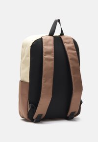 Zaino con parte superiore color crema, parte inferiore marrone e spallacci in rete nera. Presenta una finitura testurizzata e fibbie regolabili sugli spallacci.