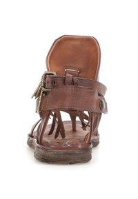 Brune lædersandal med åben bagside, justerbare stropper og lynlåsdetalje. Tekstureret sål med synlig slid. Rund tå-design.