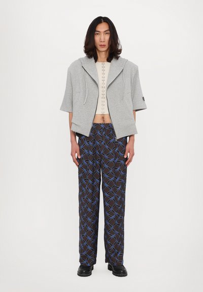 Gray cropped hoodie with a large hood and front zipper, paired with dark patterned wide-leg pants featuring blue geometric lines. Black footwear.