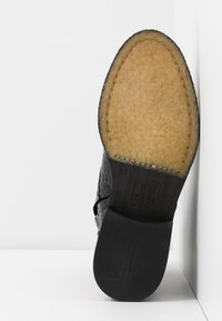 Scarpa nera in pelle con finitura texture e suola in pelle. Presenta una soletta di colore nocciola e un logo discreto impresso sulla suola.