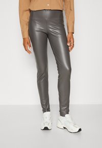 Grijze faux leren legging sluit nauw aan op het lichaam, met een gladde textuur en hoge tailleband, gecombineerd met witte en grijze sneakers.