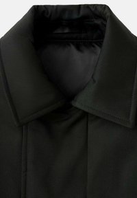 Abrigo negro con un amplio collar, que presenta un exterior suave y texturizado y un forro interior brillante. Líneas limpias sin hardware ni patrones visibles.