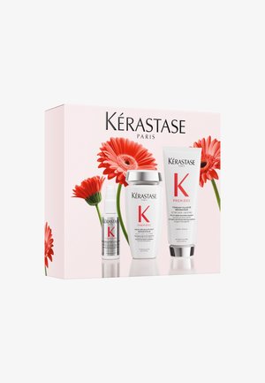 Set de soins capillaires Kérastase Paris Première avec shampooing, après-shampooing et tubes de traitement, décoré de fleurs de gérbera rouges sur l'emballage.