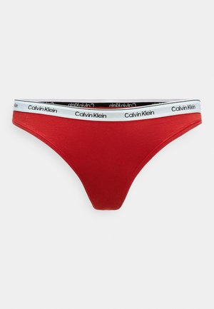 Tanga in cotone rosso con un design a vita bassa. Presenta un elastico con marchio bianco e nero. Texture liscia e stile minimalista.
