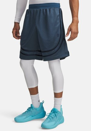 Heren basketbalshorts in marineblauw mesh met zwarte strepen. Voorzien van een elastische tailleband en zakken. Draagt over witte legging en turquoise sneakers.
