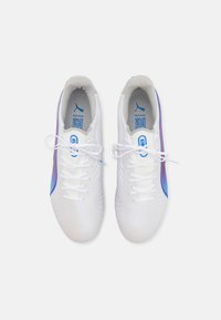 Zapatillas deportivas blancas con parte superior texturizada, cierre de cordones, acentos prominentes en púrpura y azul en el lateral, y diseño de puntera reforzada.