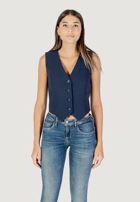 Gilet marine avec un décolleté en V profond, cinq boutons et une poche sur la poitrine à gauche ; associé à un jean skinny bleu clair, au design ajusté.