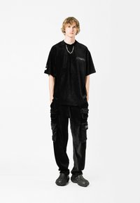 Camiseta de corte oversize de pana negra con bolsillo en el pecho, combinada con pantalones cargo a juego con bolsillos laterales y calzado texturizado negro.