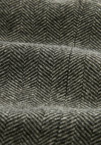 Tissu en laine au motif chevron, présentant des nuances de gris et de noir. Texture douce avec des fibres visibles et un subtil éclat.