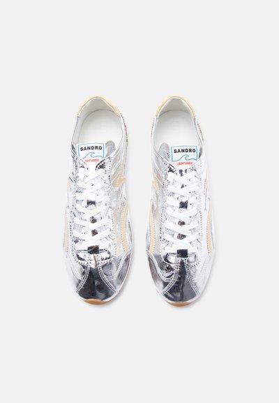 Ζεύγος αθλητικών παπουτσιών από ασημί μεταλλικό υλικό με λευκά κορδόνια, μπεζ λεπτομέρειες και ετικέτα "Sandro Light Wave" ορατή στη γλώσσα κάθε παπουτσιού.