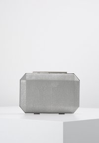 Rectangular silver clutch with a textured metallic mesh surface and a slim top clasp, placed on a white pedestal against a plain background.