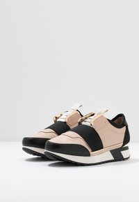 Baskets noires et roses avec un mélange de cuir et de suède. Dotées de sangles élastiques, de garnitures en or et d'une semelle noire texturée.