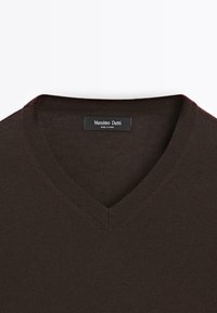 Maglione marrone a V realizzato in un tessuto a maglia fine. Presenta una consistenza liscia con rifiniture a costine attorno al colletto e un'etichetta del marchio all'interno.