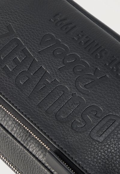 Μαύρο πορτοφόλι από υφή δέρματος με ανάγλυφο λογότυπο "DIESEL 1995" και ορατό ασημένιο φερμουάρ σε ανοιχτό φόντο.