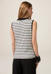 Mouwloze top met zwart-wit gestreept patroon en een polokraag. Heeft een aansluitend design en een gladde textuur, gecombineerd met zwarte broeken en een gehaakt armband.