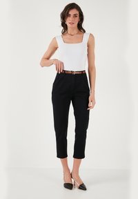 Top bianco a coste con scollo quadrato abbinato a pantaloni neri a vita alta e scarpe con tacco bicolore nere e beige. La cintura presenta una fibbia metallica.
