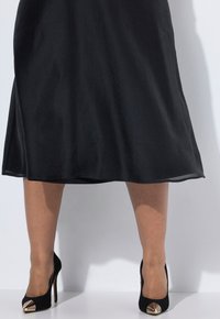Jupe noire en ligne A avec un léger éclat, associée à des chaussures à talons hauts noires avec un embout en métal doré à motif.