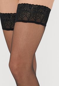 Čierne čipkové pančuchy s vysokým strihom a zakriveným dizajnom a priesvitným nylonovým telom. Čipka má kvetinový vzor pre väčší detail.