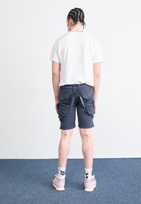 Svarte cargo shorts med flere lommer og stropper, kombinert med en hvit t-skjorte og rosa joggesko med hvite såler og svarte detaljer.