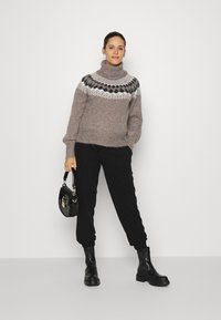 Pullover de lã castanho com gola alta e padrão fair isle em preto e branco, combinado com calças tapered pretas e botas de tornozelo pretas.