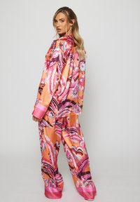 Set di abbigliamento da casa in satin con vivaci motivi astratti in rosa, arancio e nero. Include una camicia dal taglio morbido con polsini rosa e pantaloni abbinati.