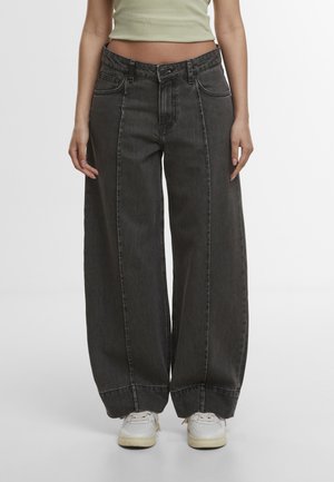 Wide-leg black denim jeans worn with white sneakers and a light green cropped tank top, shown from waist to feet.