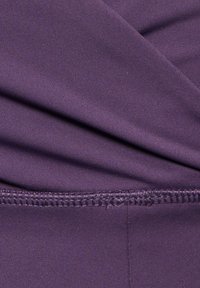 Fioletowy materiał o gładkiej fakturze, z fałdami i detalami szwów na dolnym brzegu. Materiał wydaje się elastyczny i lekki.