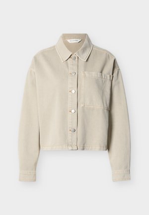 Giacca corta in denim beige con bottoni a pressione argentati, colletto a punta, maniche lunghe e una tasca sul petto sul lato sinistro.