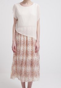 Hellästi laskeutuva, kermaisenvärinen mekko, jossa on läpikuultava päällikerros ja oranssin ja sinisen sävyinen kukkakuosi hameosassa, polvipituinen ja pyöreällä pääntiellä.