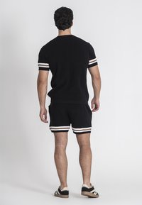Completo di top e pantaloni shorts in maglia nera con righe bianche e arancioni sulle maniche e sull'orlo. Le scarpe sono nere con dettagli crema.