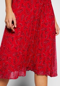 Rotes Kleid aus einem leichten, fließenden Stoff mit einem Paisleymuster in Schwarz-weiß-Akzenten und Falten in der Nähe des Saums.