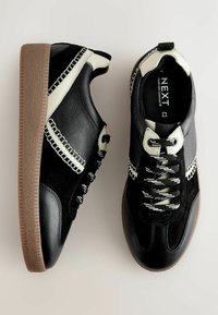 Schwarze und graue Sneaker aus Leder und Wildleder, mit kontrastierenden Akzenten, genähten Details und strukturierten Gummisohlen.