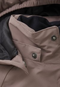 Ljusrosa jackkrage med svart foder; har silverfärgade tryckknappar och sömnadsdetaljer. Texturerad tyg med en mjuk yta.